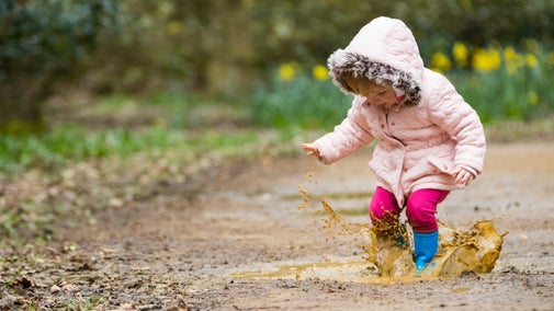 A child in wellies jumps in a muddy puddle.